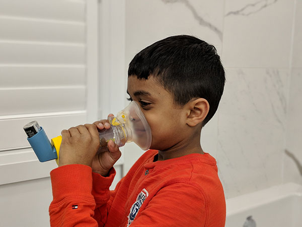 Child using an age-appropriate valved spacer device with an asthma inhaler. 
