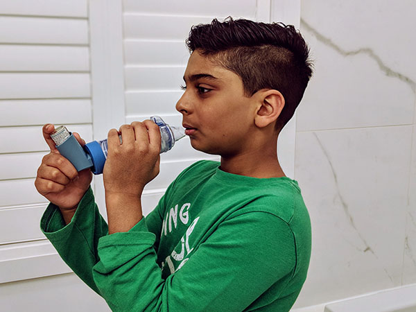 Child using an age-appropriate valved spacer device with an asthma inhaler.
