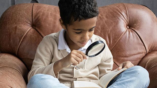 Child looking at a book with a magnifying glass