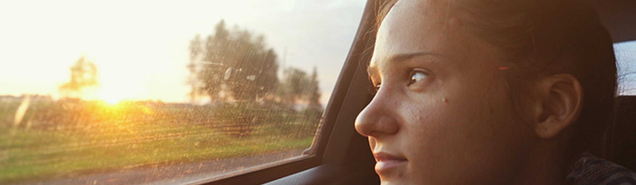 Teenager looking out the window of a car into the sunset 
